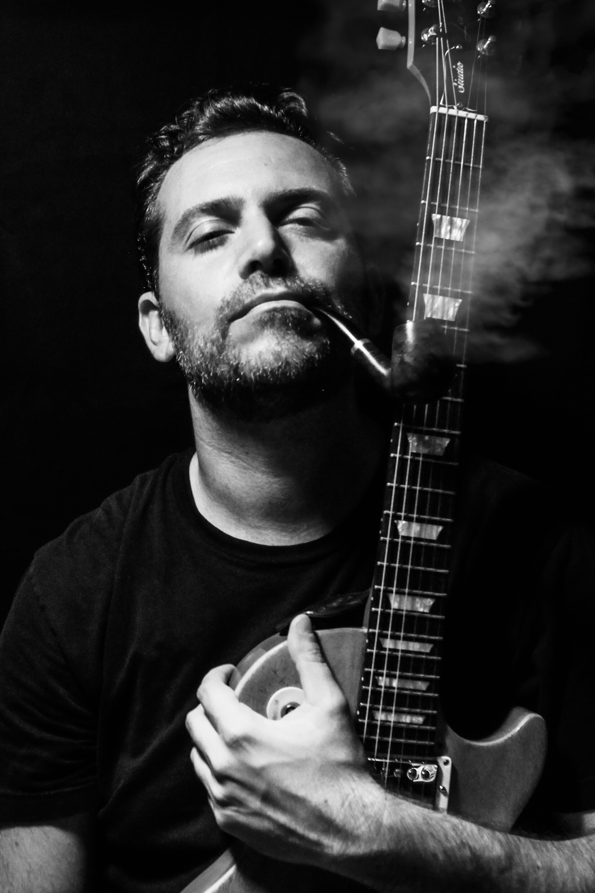 Peter Soros holding a Les Paul guitar, pipe in mouth, black and white portrait